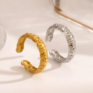 Floral embossed stainless steel open rings in gold and silver finishes on a beige background