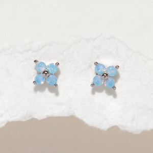 Detailed shot of light blue four-leaf clover stud earrings with opal texture on white paper