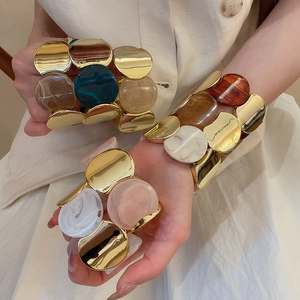 Détail de bracelets superposés en résine marbrée et métal doré sur le poignet