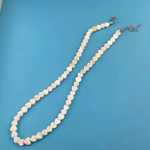 Detail view of a white heart-shaped bead necklace with a metal lobster clasp and chain