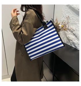 Detail of blue and white striped canvas tote bag with black handles held by model