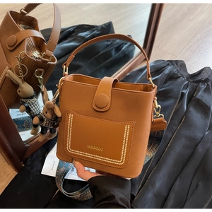 Detail of retro brown bucket bag with wide ethnic strap, gold rivets and bunny charm