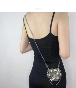 Silver flower-shaped metal crossbody bag with bead chain strap on model in black dress