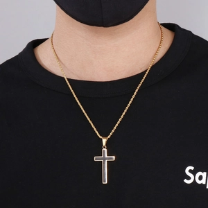Detail of hip hop style gold and black cross pendant on a rope chain worn by a male model