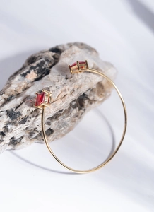 Detailed shot of golden open bracelet with red square-cut zircon gems on a stone