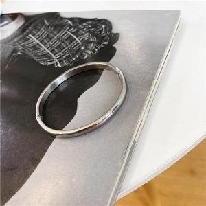 Detailed view of silver minimalist oval bangle with hinge closure on fashion magazine
