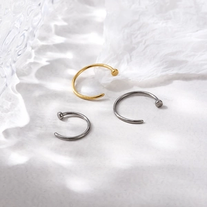 Macro shot of gold and silver G23 titanium C-shaped nose rings on textured glass