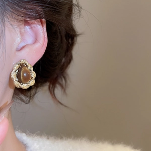 Macro close-up of a twisted gold textured earring with a brown tiger eye gemstone