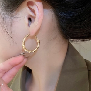 Detailed close-up of golden twisted rope hoop earrings worn by a model in soft lighting