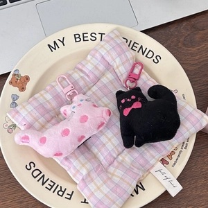 Close-up of cute plush cat keychains in pink and black on a checkered pillow