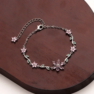 Macro shot of silver cherry blossom bracelet with pink floral gems and green leaf accents