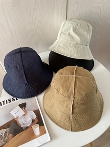 Flat lay of nylon bucket hats in navy, khaki, beige, and black on a white table