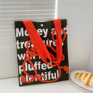 Close-up of green knit tote bag with orange handles and white typography on a table