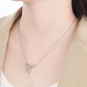 Close-up of a silver bow necklace with sparkling crystals worn by a model in a beige suit