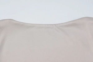 Detail of light beige ribbed knit fabric showing the square neckline and fine texture