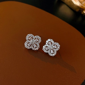 Macro shot of silver four-leaf clover stud earrings with zircon inlay on leather