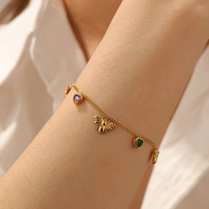 Close-up of gold chain bracelet with bee charm and purple green heart stones on wrist