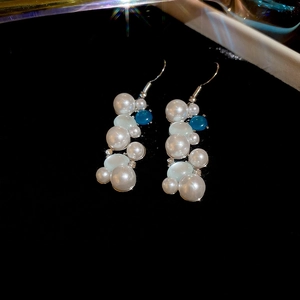 Close-up of elegant long cluster pearl earrings with blue beads and silver metal hooks