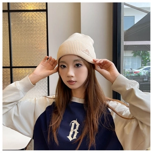 Detailed view of a cream knitted beanie worn by a model in a cozy cafe setting.