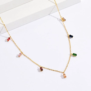 Close-up of golden necklace with colorful rectangular zircon gemstones on beige stand