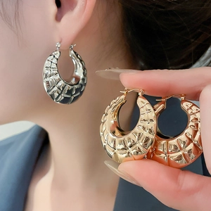 Close-up of golden chunky hoop earrings with textured geometric pattern on a model