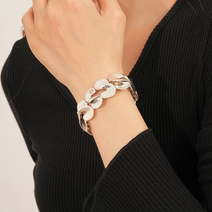 Close-up of a silver organic S-link metal bracelet worn by a model in a black outfit