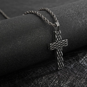 Detailed macro view of black punk style cross pendant with intricate woven texture on a rope chain