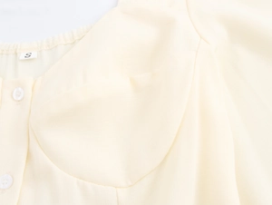 Detail of light yellow French square neck dress showing fabric texture and white buttons