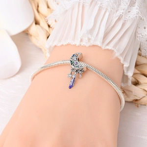 Detailed view of silver crescent moon charm with multi-color stones and purple feather on a bracelet