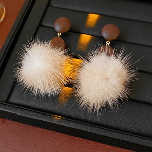 Detail view of round brown wooden studs and white fur ball earrings with gold connectors