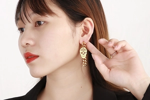 Macro detail of a gold hollow skull drop earring with a chain on a female model