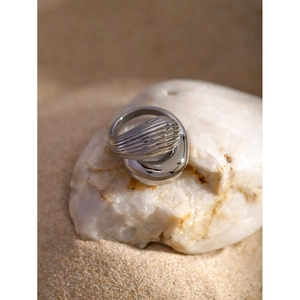 Close-up of a silver wavy stacked ring placed on a white stone with a sandy background