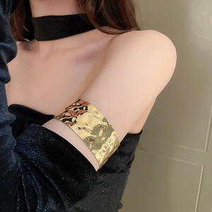 Detailed view of wide gold metal arm cuff featuring irregular hammered texture on model