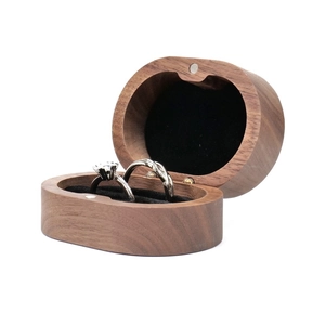 Close-up of walnut wood ring box with black lining and silver rings on white backdrop
