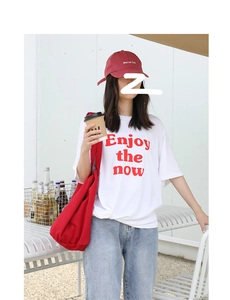 Outdoor view of a red canvas shoulder bag styled with a white slogan tee and vintage denim
