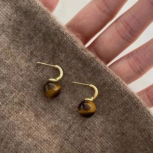 Detail of gold-plated hoop earrings with brown tiger eye stones on knit fabric