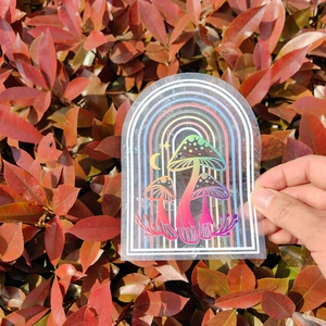 Rainbow arch and mushrooms suncatcher window sticker shown against autumn leaves