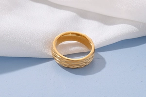 Macro shot of gold stainless steel ring with geometric faceted texture on white silk fabric
