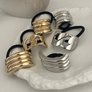 Detail view of various gold and silver metal hair rings arranged on a white ceramic plate