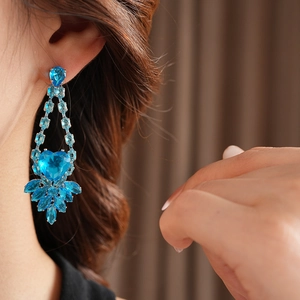 Close-up of heart-shaped blue rhinestone earrings with large center gemstone on model