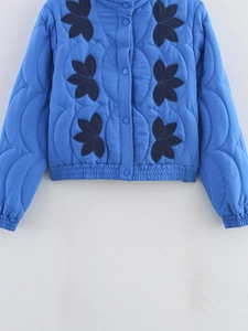 Detailed view of women's royal blue quilted jacket featuring floral embroidery and snap buttons