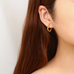 Close-up of gold heart-shaped hoop earring worn by a model with brown hair