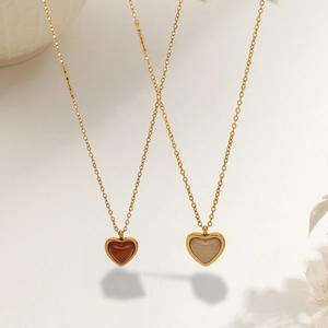 Detail of two gold-finish heart necklaces with red and beige resin stone pendants