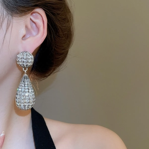 Detailed close-up of silver teardrop dangle earrings with rhinestones on a model's ear