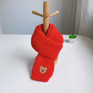 Detail of red cable knit kids scarf featuring a cute bear patch on a wooden hanger