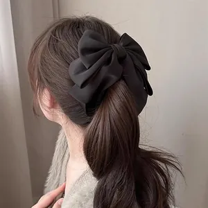 Detail of a large black matte satin bow hair clip styled on a ponytail for a high-end look
