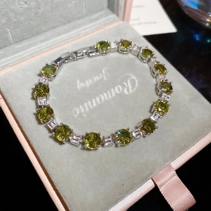 Detail of a luxury tennis bracelet with olive green stones in a grey velvet gift box