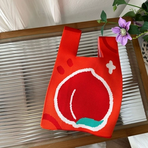 Close-up of red knitted tote bag featuring a peach pattern on a textured glass table
