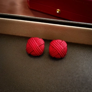 Macro shot of red knot stud earrings with woven texture on a premium dark velvet lining