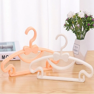 Bowknot plastic kids hangers in orange pink and white on a wooden tabletop